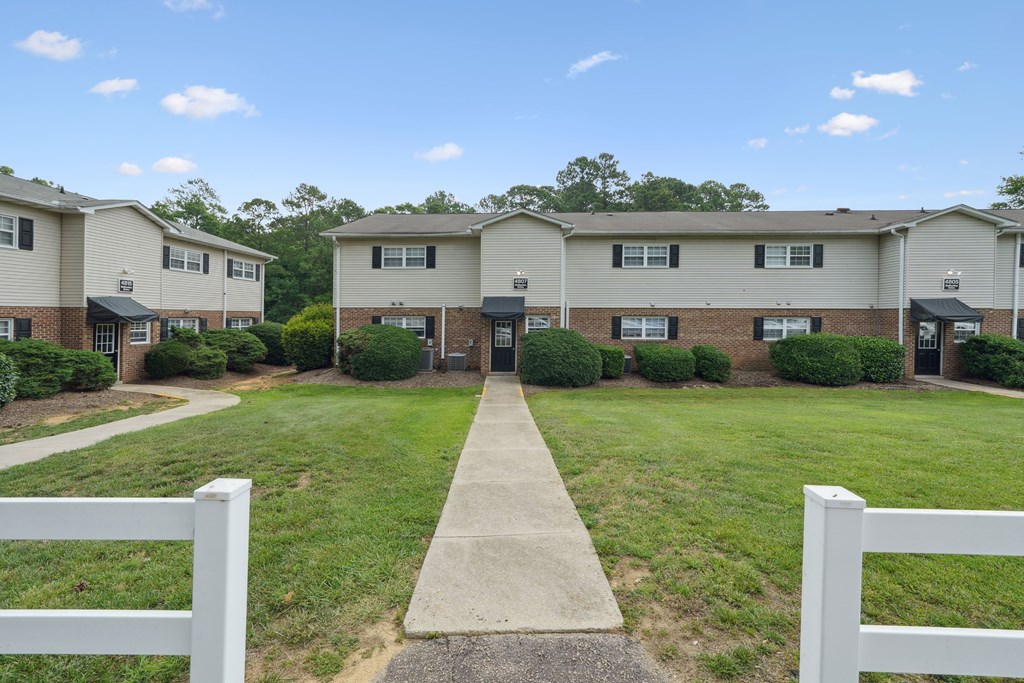 A white picket fence surrounds a grassy area in front of a row of houses.