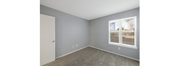A room with a carpeted floor, a window with blinds, and a door.