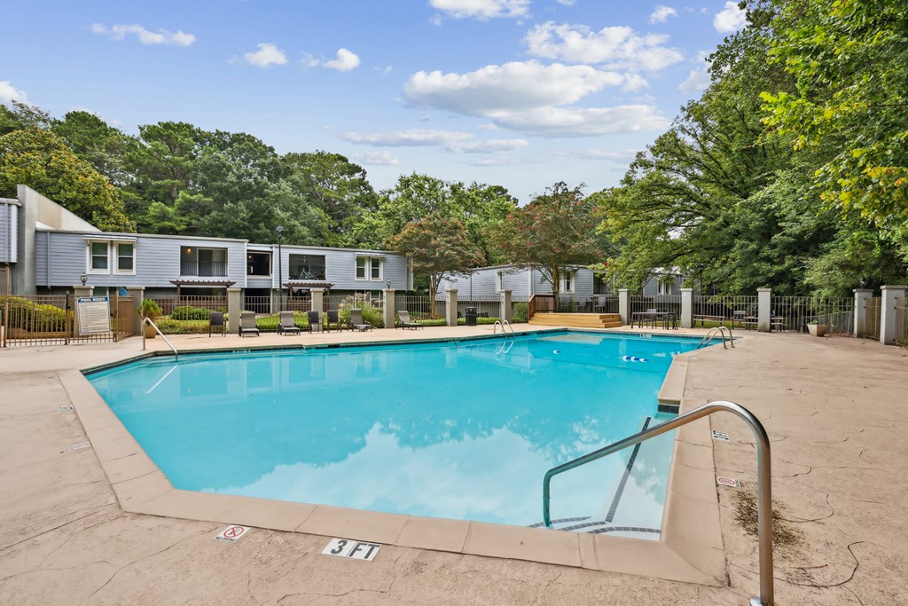A swimming pool surrounded by trees and a building in the background.