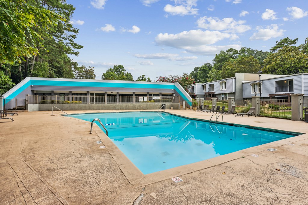 A large outdoor swimming pool with a diving board and a small building in the background.