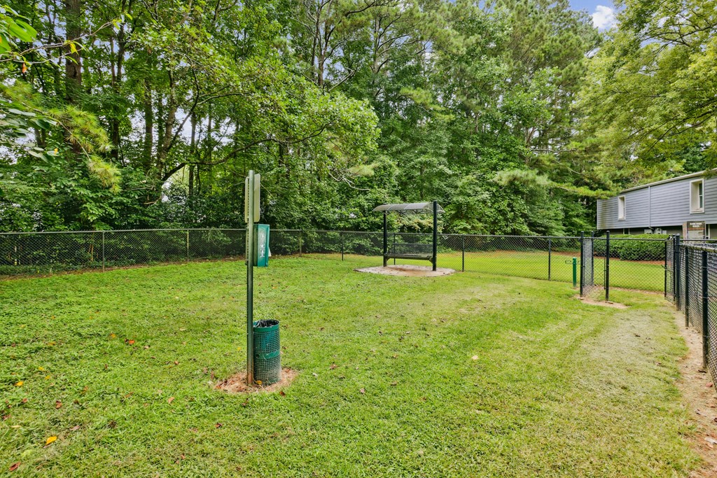 A green pole stands in a grassy field with a fence and trees in the background.