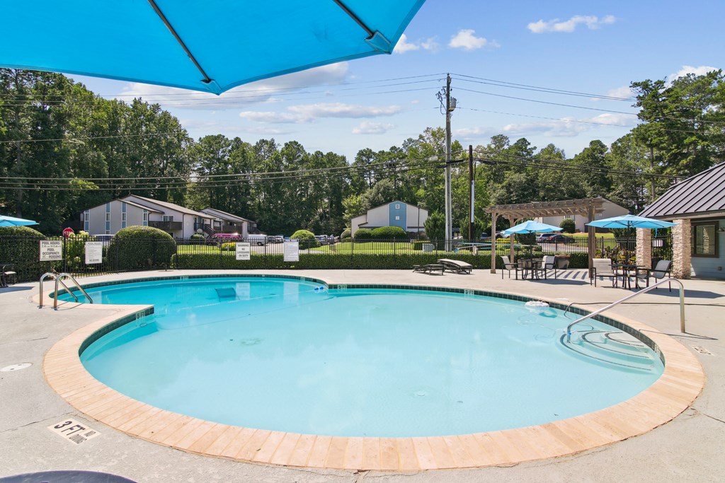 A round swimming pool with a blue umbrella above it.