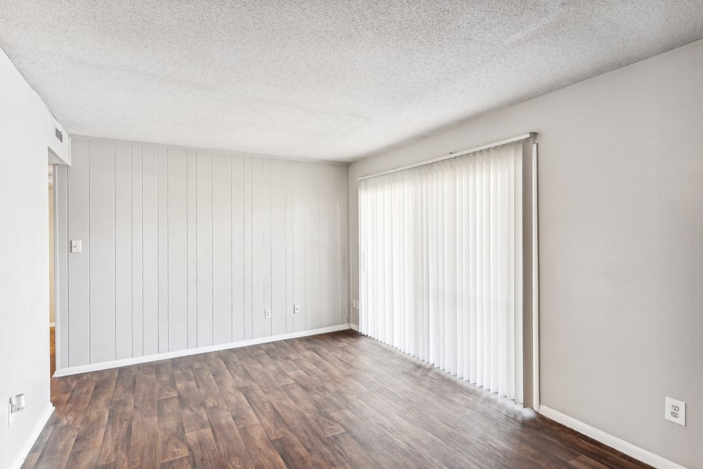 the living room of an apartment with wood flooring and white walls and sliding doors