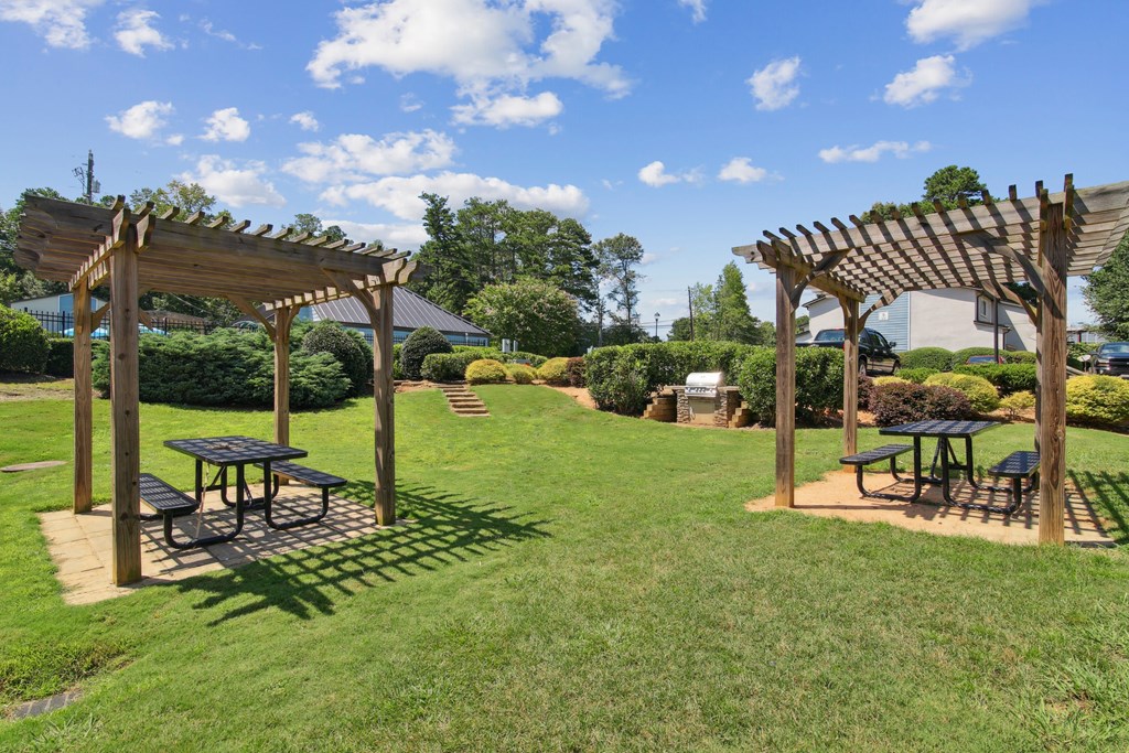 A sunny day at a park with picnic tables and pergolas.