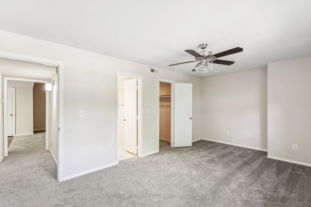 an empty bedroom with a ceiling fan and closets