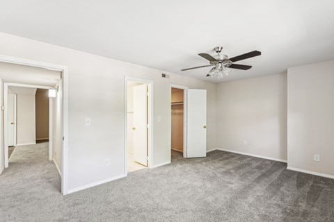 an empty bedroom with a ceiling fan and closets