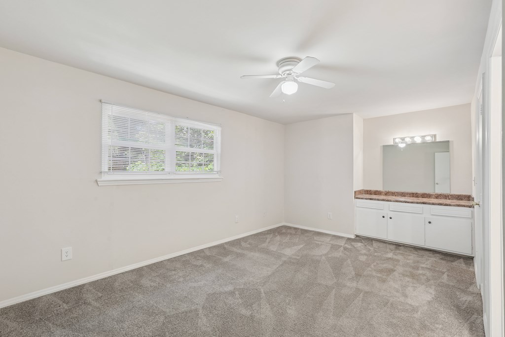 A room with a carpeted floor, a ceiling fan, and a window with blinds.