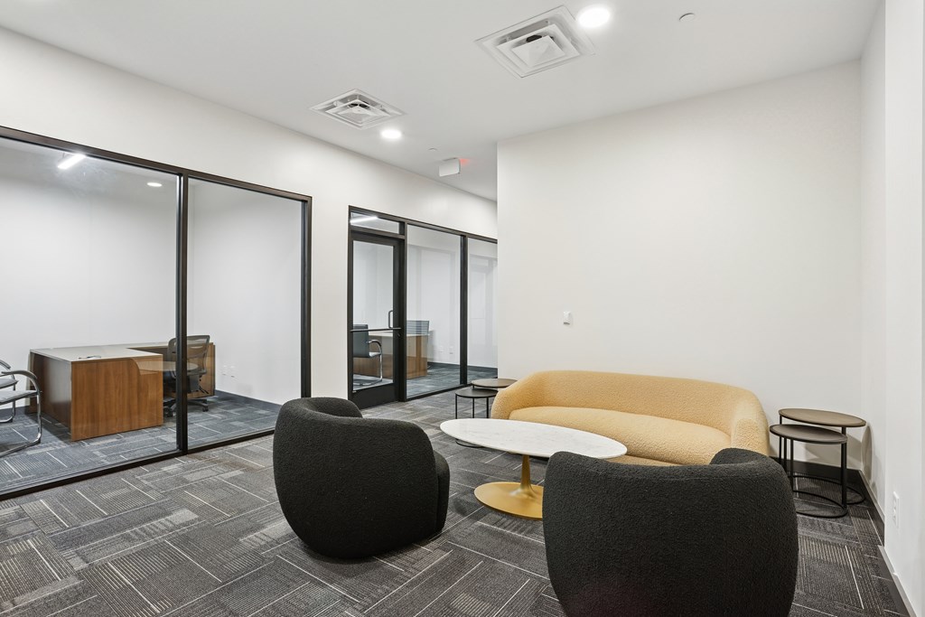 A modern office space with a grey carpet, a yellow sofa, a black chair and a wooden table.