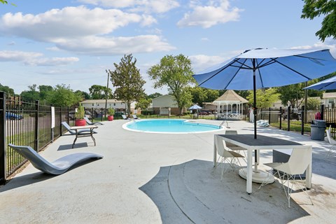 A pool area with a table and chairs and a blue umbrella.