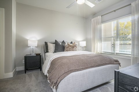 A bedroom with a large bed and a window with blinds.