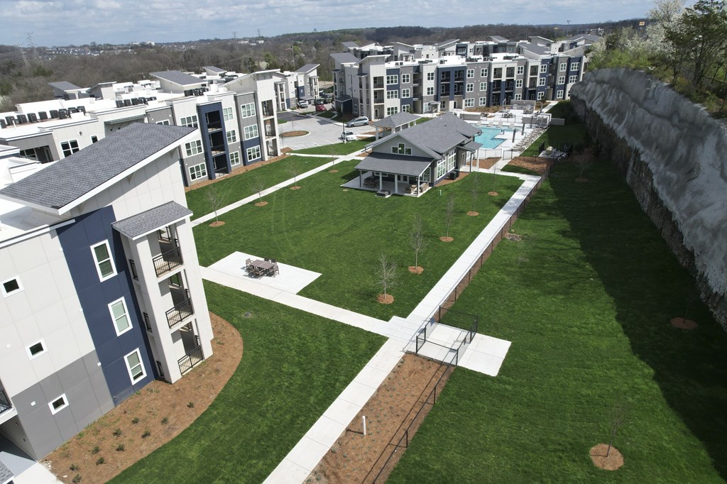 A large grassy area with a white pathway and a small building with a pool at The Percy Apartments, Nashville, TN, 37214