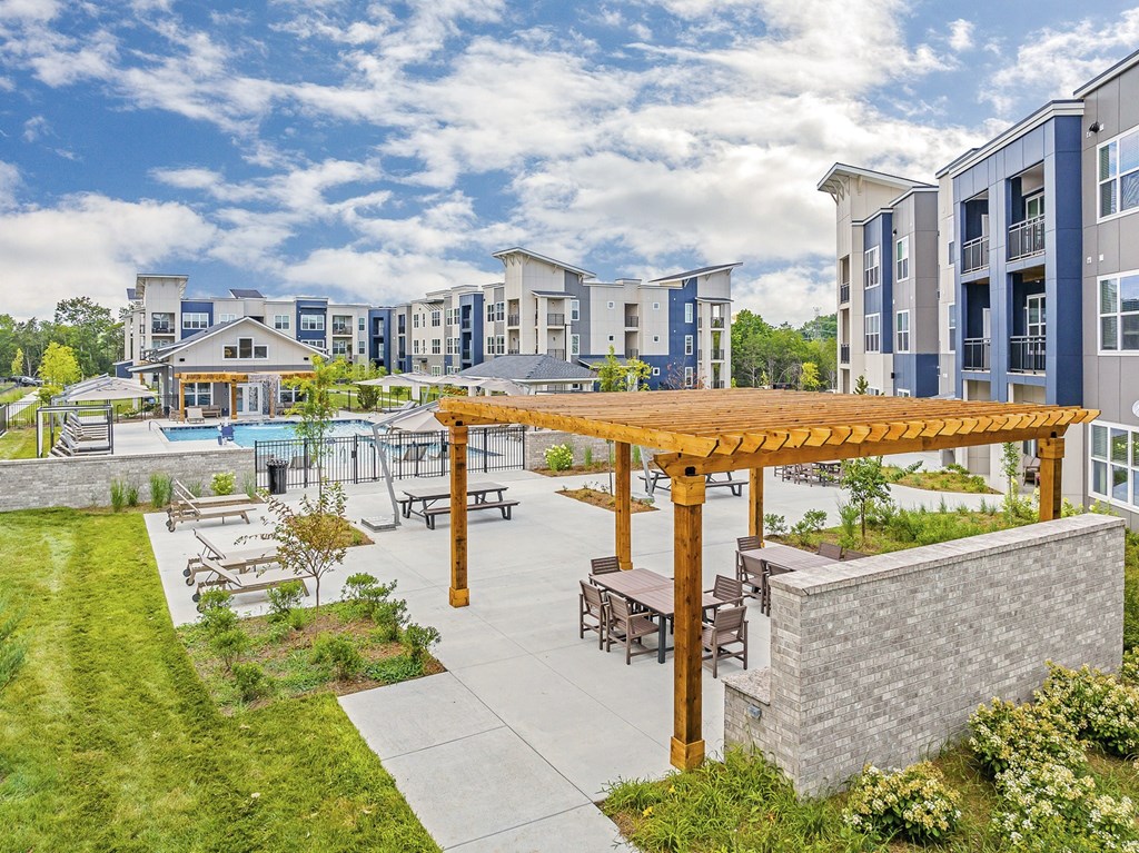 A large outdoor patio area with a wooden pergola and seating area in front of apartment buildings at The Percy Apartments, Nashville, TN, 37214