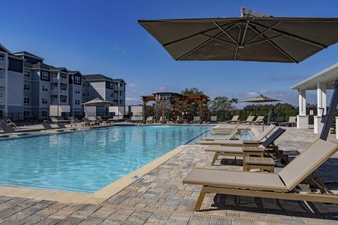A pool with sun loungers and a building in the background at The Waverly at Winter Haven Apartments, Florida, 33884