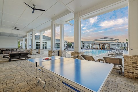 A table tennis table is in the middle of a room with a pool table and a table fan.