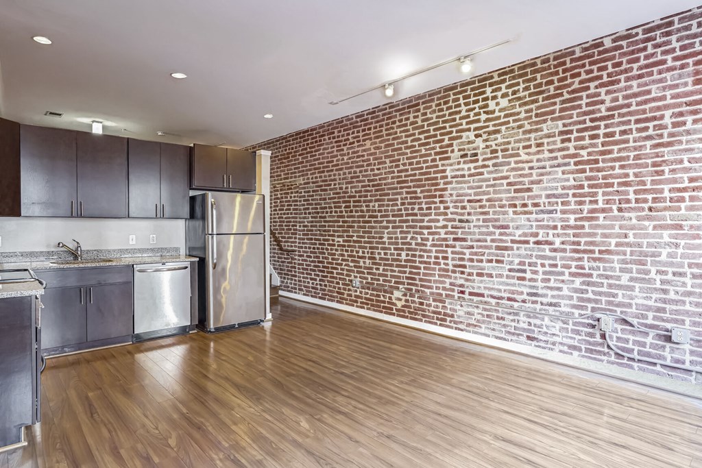 a living room with a brick wall and a kitchen with stainless steel appliances