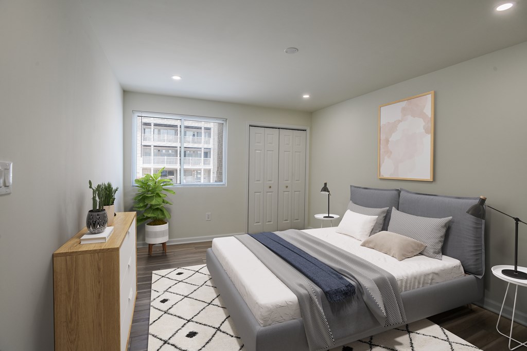 A bedroom with a bed, nightstand, and a plant.