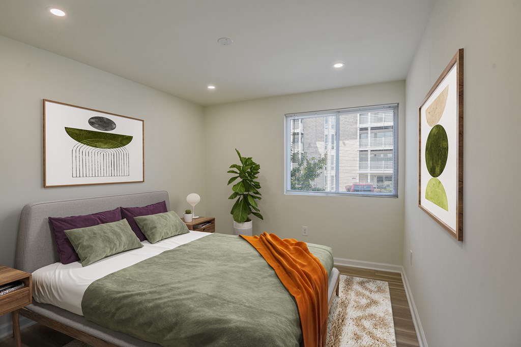 A bedroom with a bed, a potted plant, and two framed pictures on the wall.