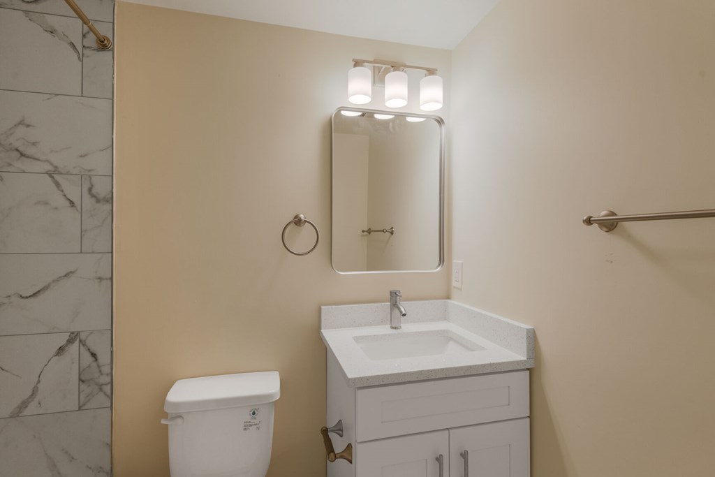 A bathroom with a toilet, sink, mirror and a towel bar.