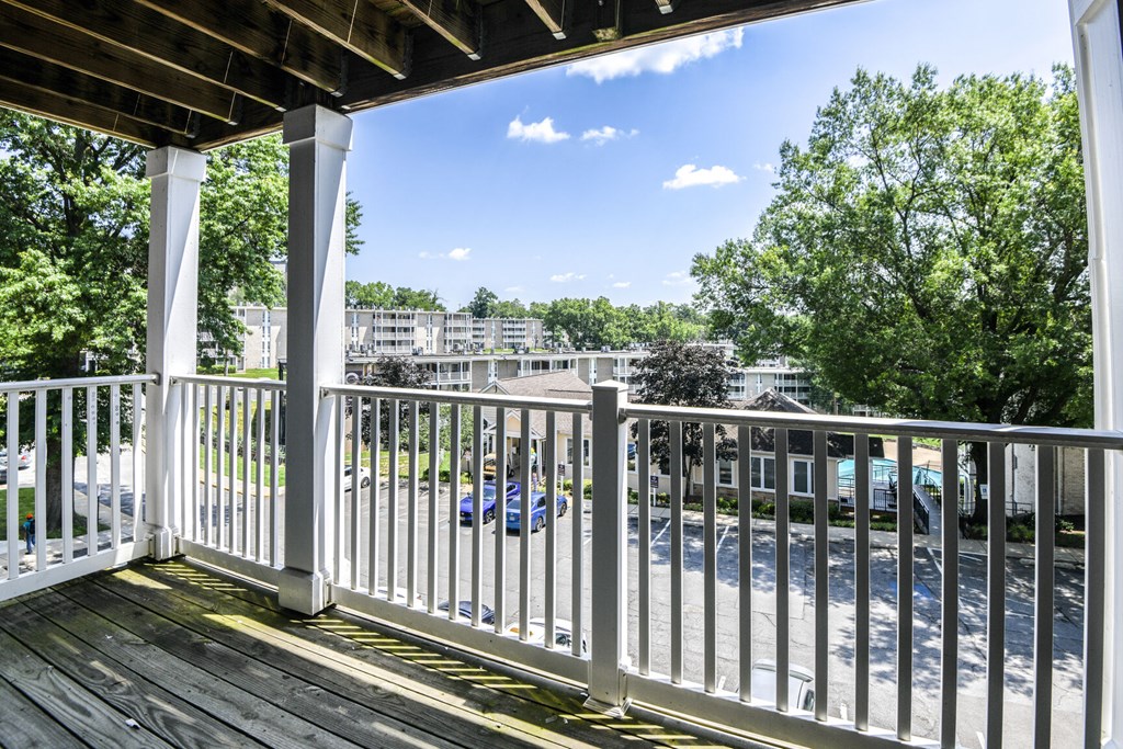 A white railing on a wooden deck overlooks a parking lot.
