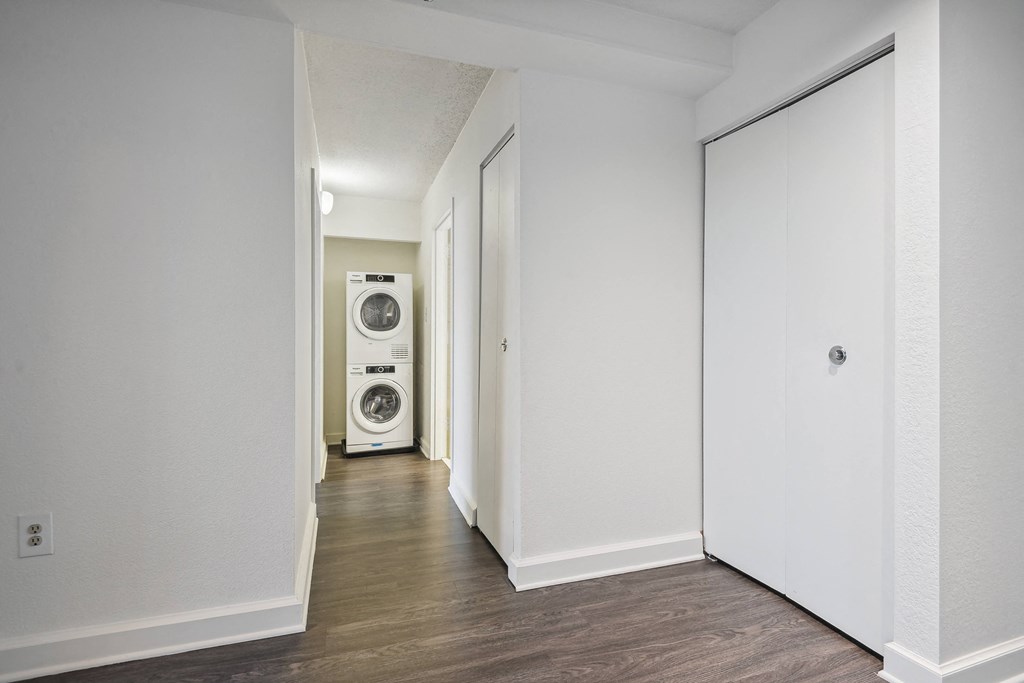 an empty hallway with white walls and a washing machine in the distance