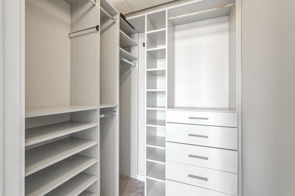a walk in closet with white shelves and a window