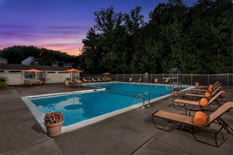 a swimming pool with chairs around it at sunset