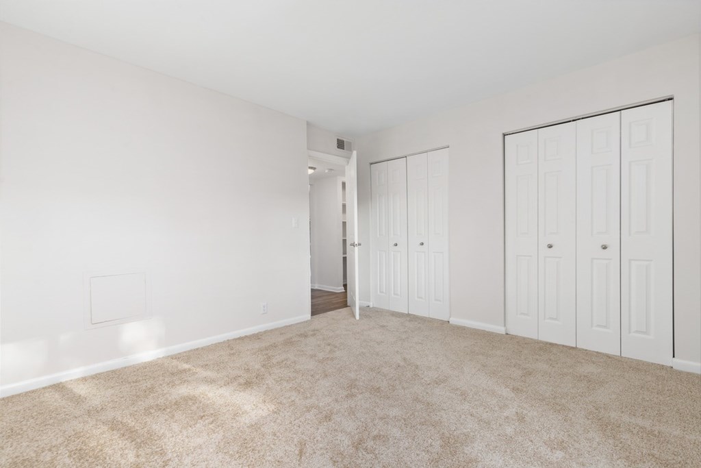 A room with white walls and carpeted floor with a doorway leading to another room.