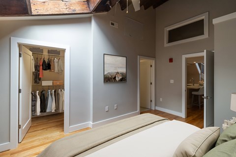 A bedroom with a large bed and a closet with clothes hanging.