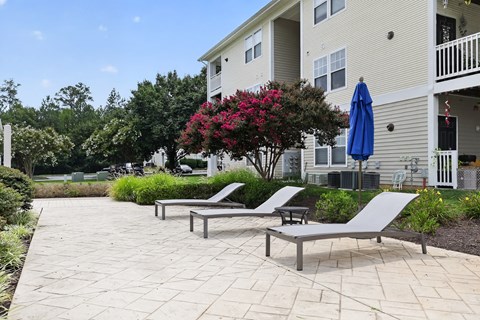A patio with two lounge chairs and a table with a blue umbrella.