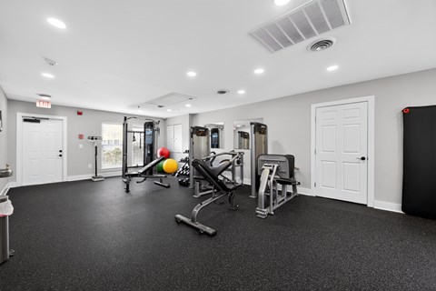 A gym with a variety of equipment including a weight machine, a bench press, and a squat rack.