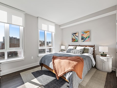 A bedroom with a large bed and a view of the city through the windows.