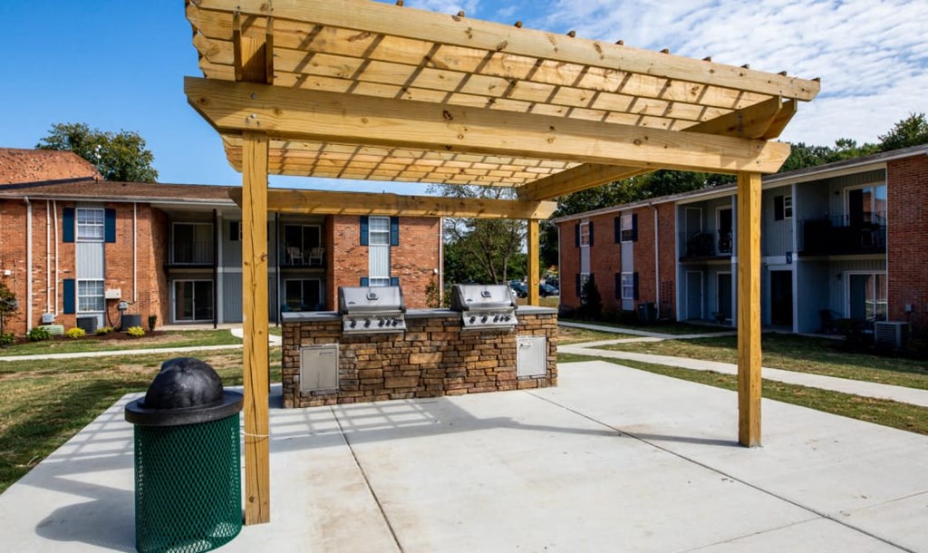 a covered patio with a grill and a trash can