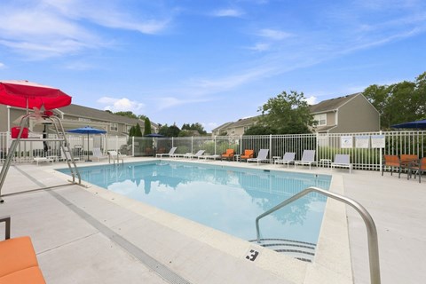 A swimming pool with a red umbrella and lounge chairs.