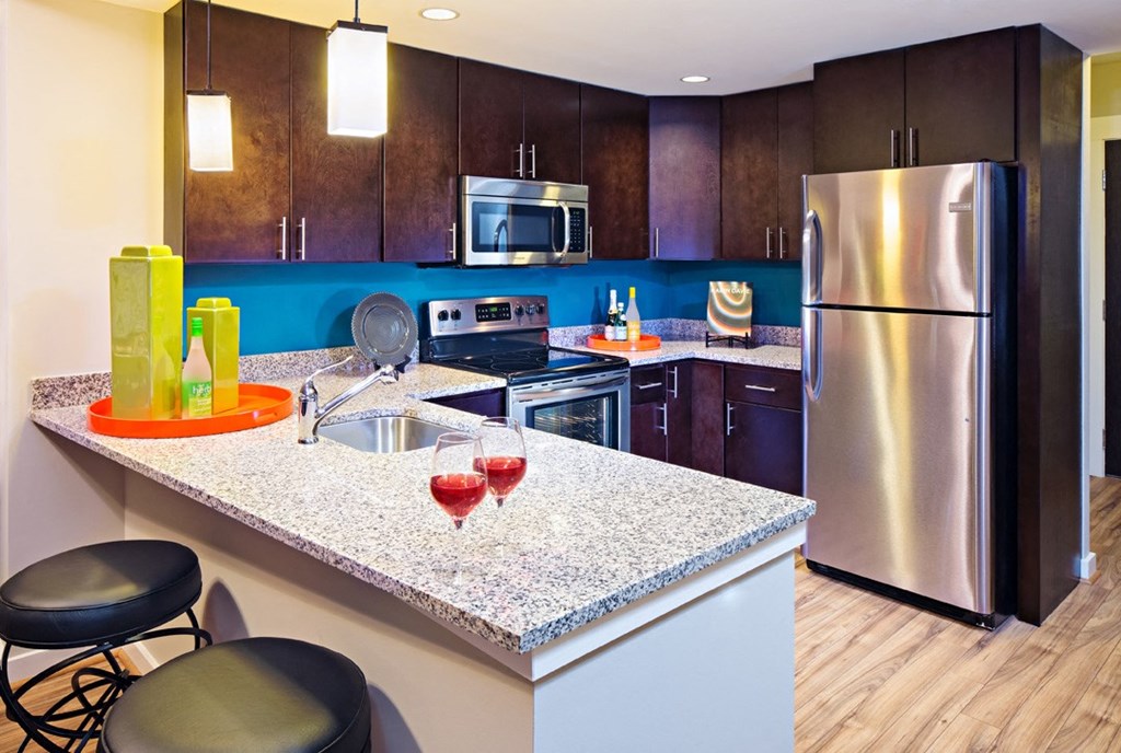 a kitchen with stainless steel appliances and a counter with glasses of red wine
