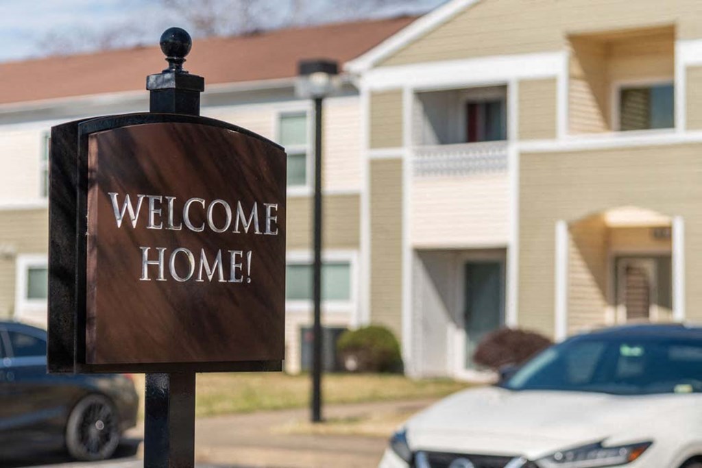A brown sign that says "Welcome Home!" stands in front of a building.
