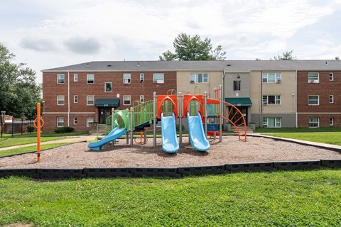 A playground with a green slide and orange safety barriers in front of a brick building.