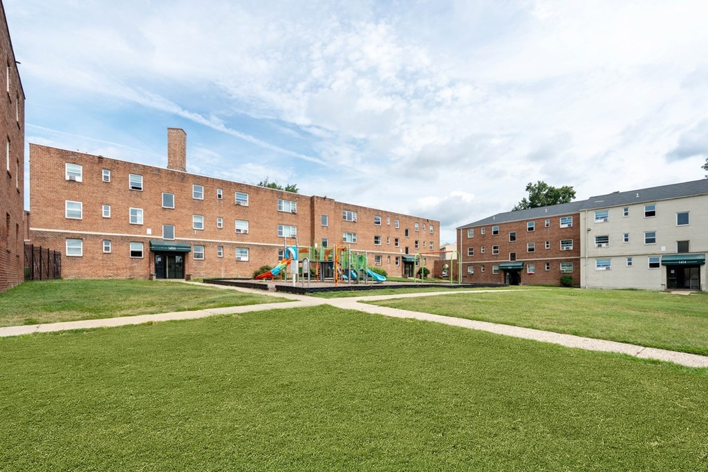 A playground in the middle of a grassy courtyard surrounded by brick buildings.