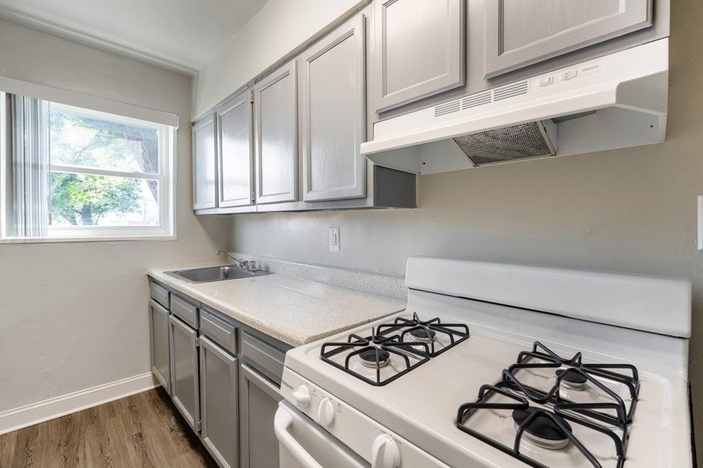 A kitchen with a white stove top oven and white cabinets.