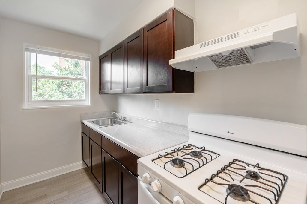 A kitchen with a white stove top oven and dark brown cabinets.
