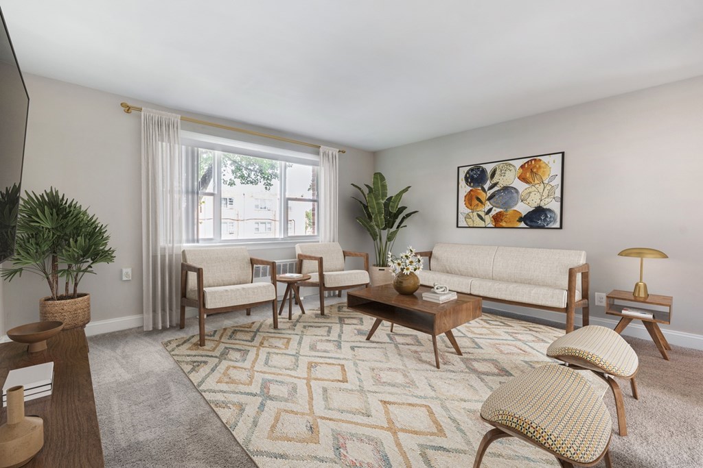 A living room with a rug, a couch, a chair, a coffee table, and a potted plant.