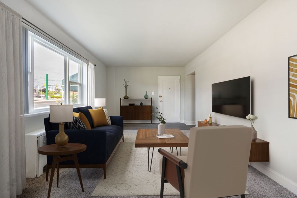 A living room with a blue couch, a wooden coffee table, and a flat screen TV mounted on the wall.