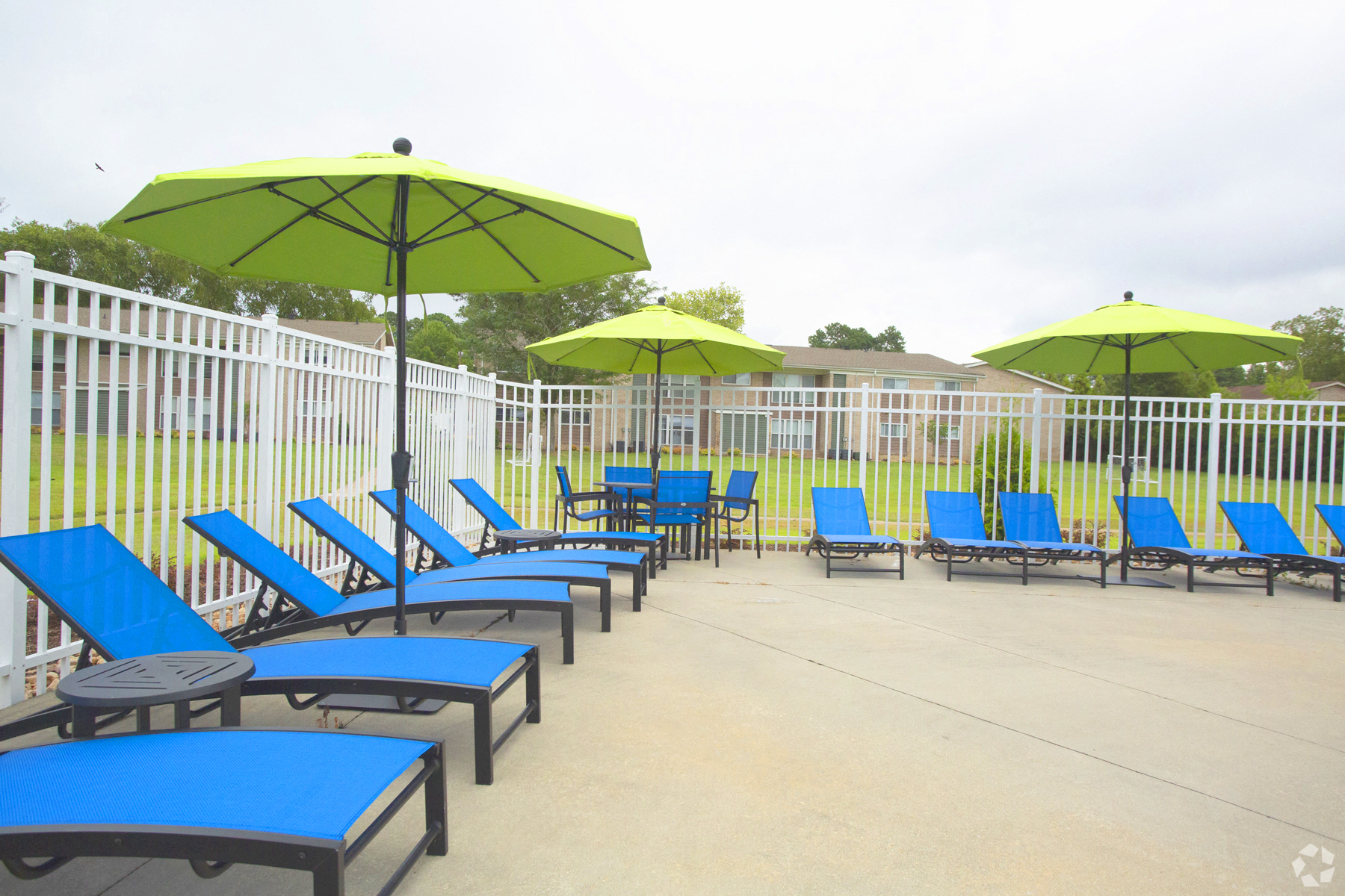 a group of blue lounge chairs with green umbrellas in front of a white fence