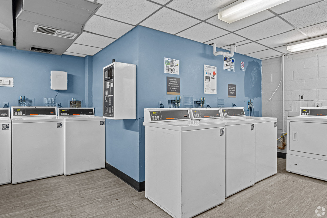 a room with light blue walls that has several washers and dryers with a coin machine