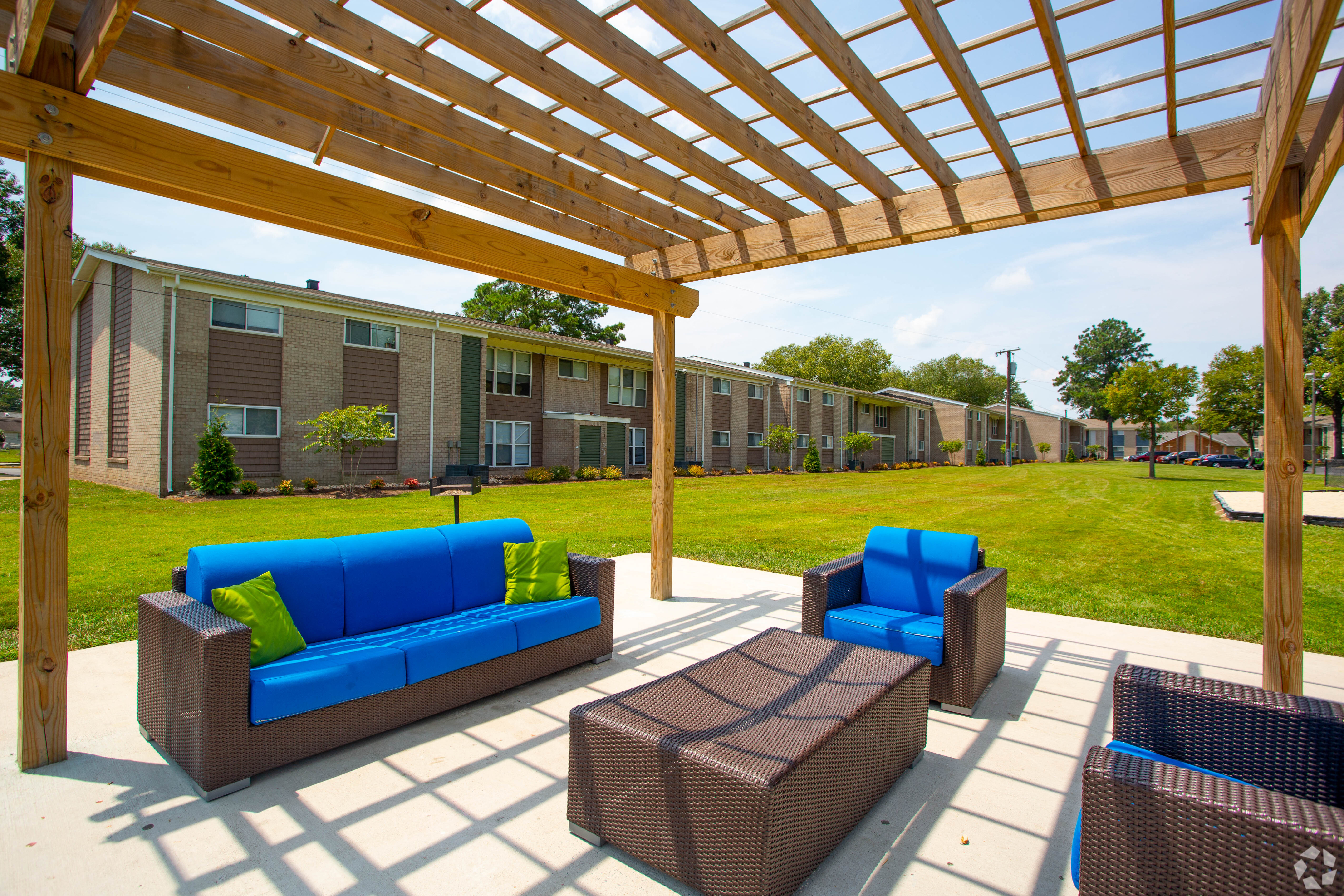 a pergola with blue couches and chairs in front of an apartment complex