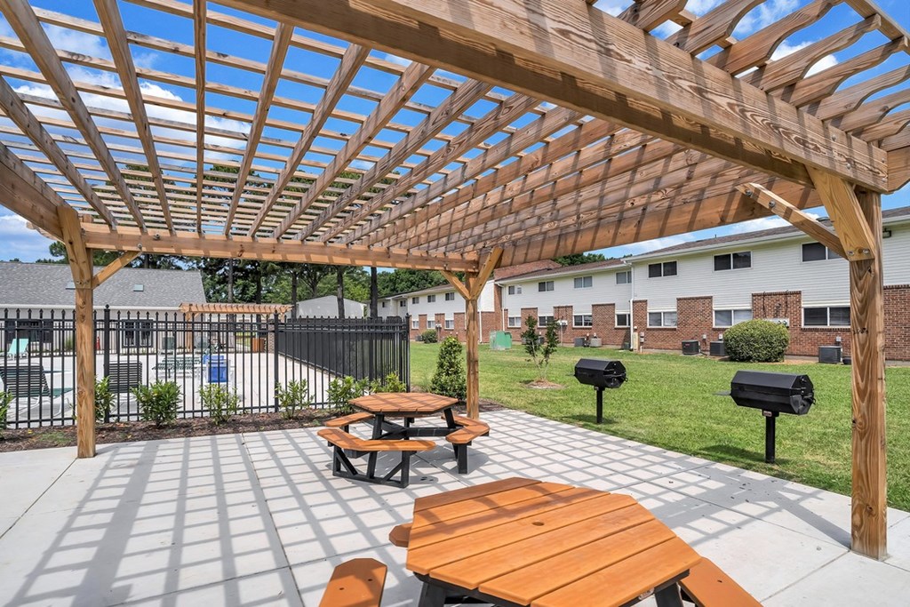 a patio with a wooden pergola and picnic tables
