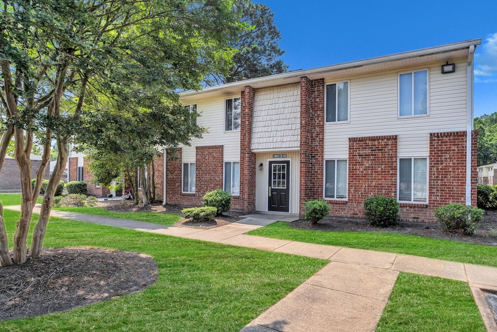 a brick and white apartment building with a sidewalk and grass