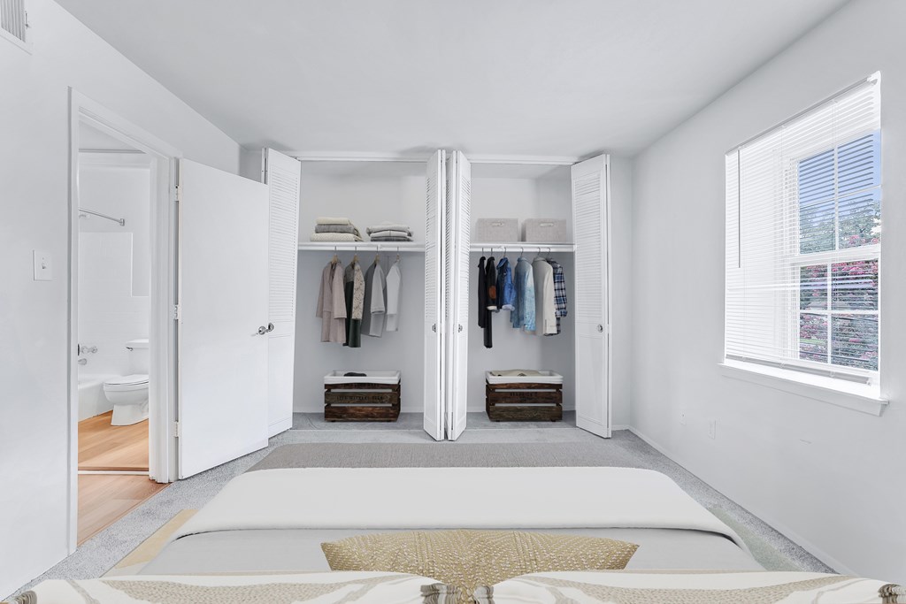 A bedroom with a large bed and a closet with clothes hanging.