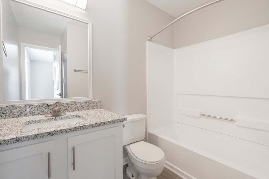 A white bathroom with a granite countertop and a toilet.