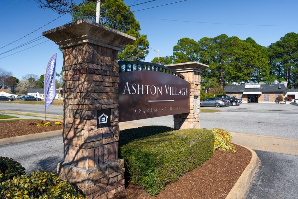 A sign for Ashton Village in front of a parking lot.