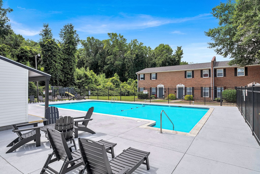 A pool surrounded by trees and chairs.